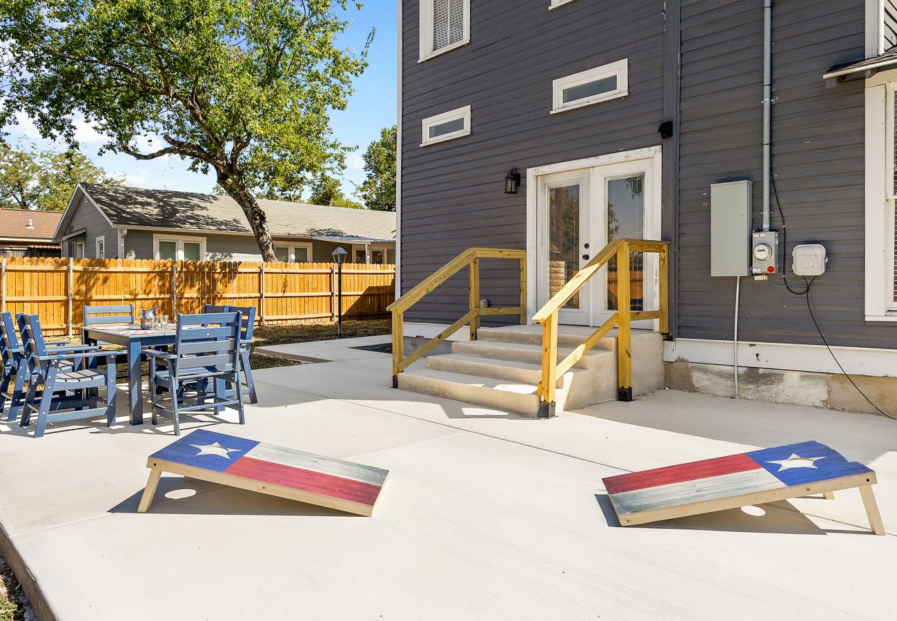 Back patio featuring blue outdoor dining furniture, Texas cornhole boards, and a fenced yard in Seguin, Texas.